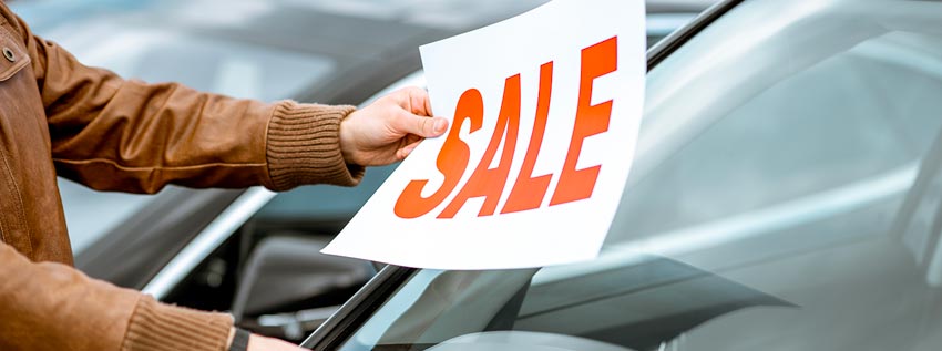 Person putting a sale sign on a used car