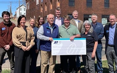Group of people holding large checks in front of property