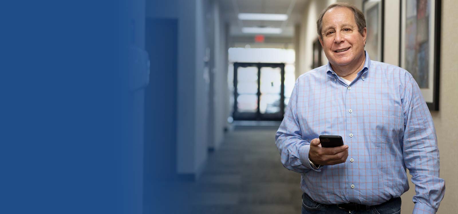 Man holding a smartphone in an office hallway with blue overlay background.