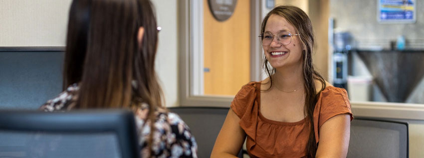 Woman siting in a Royal Office talking to a team member