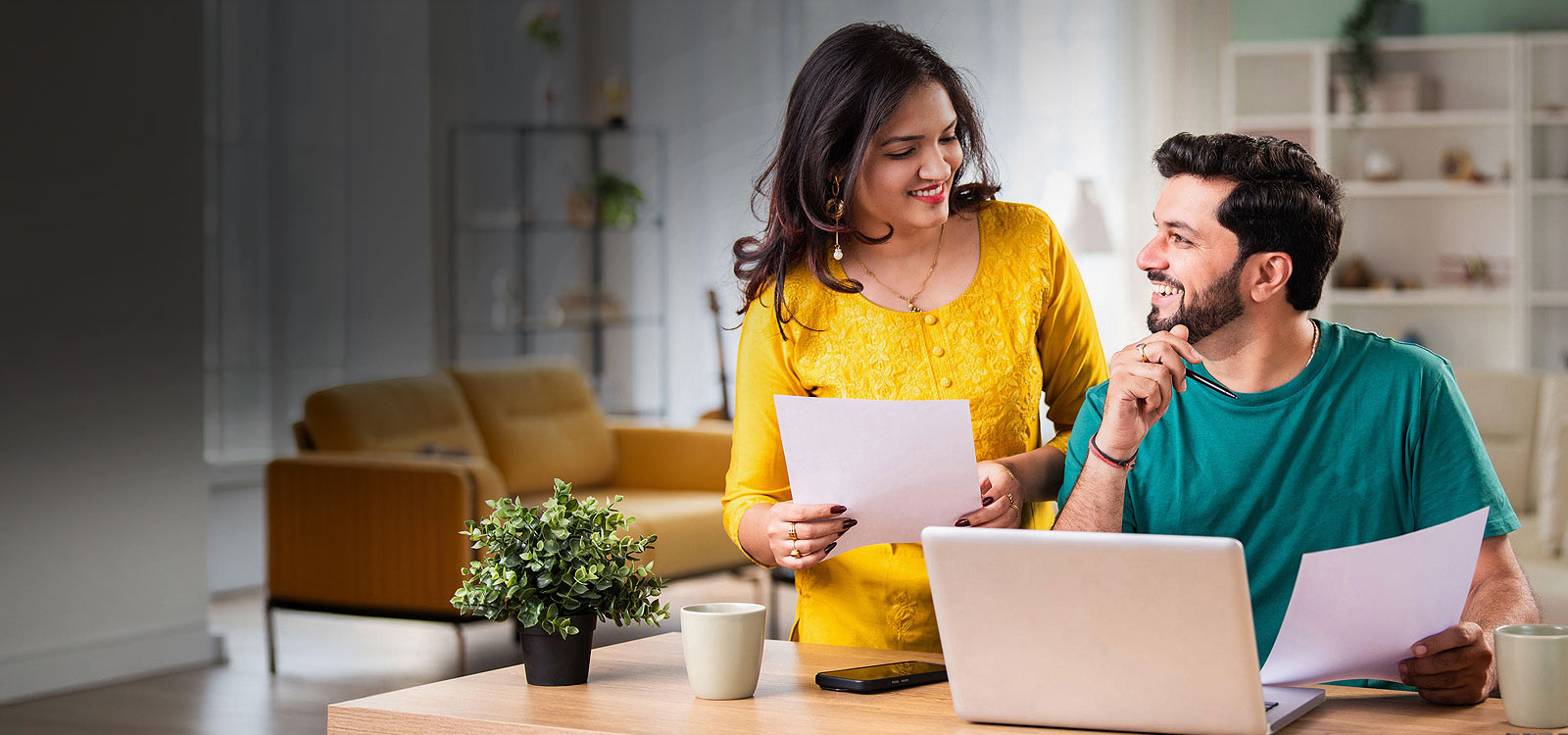 Two younger people smiling while on laptop looking at savings accounts online