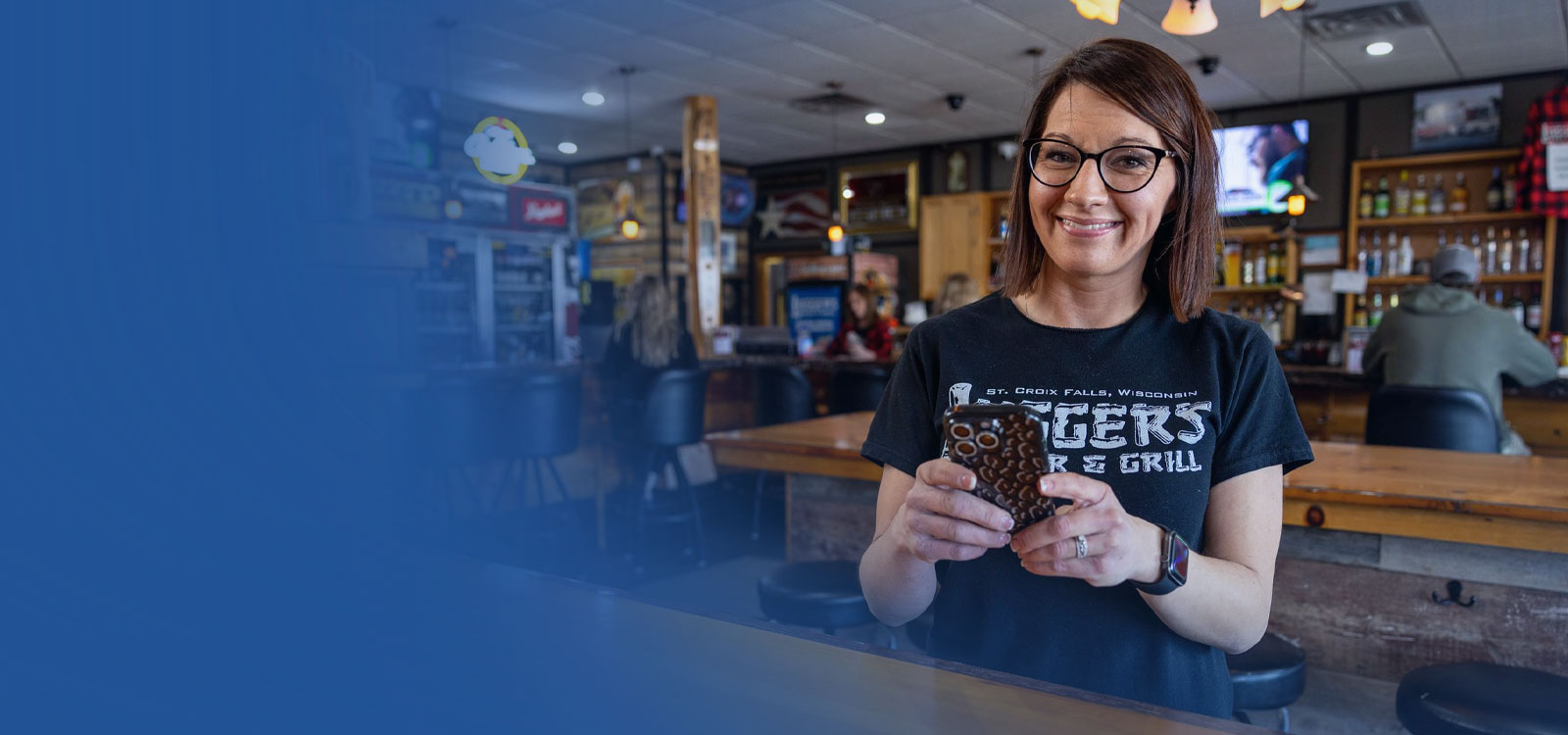 Business owner standing in her bar smiling and using a phone